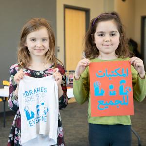 Two girls holding newly-printed "libraries are for everyone" shirts